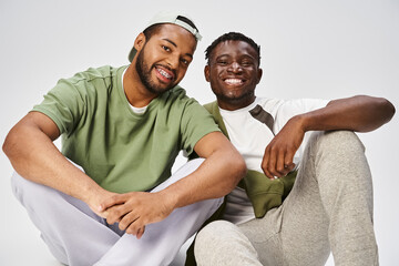 happy Juneteenth celebration, young african american man sitting with male friend on grey background