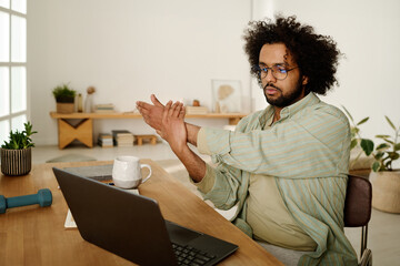 Serious young male solopreneur or freelancer looking at laptop screen while watching online video...