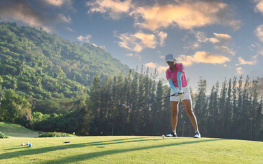 Lifestyle woman playing game golf approach tee of on the green grass mountain background. Asian female player game shot in summer