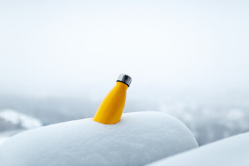 Steel thermo bottle of yellow color in snow. Close-up view. Reusable thermos.