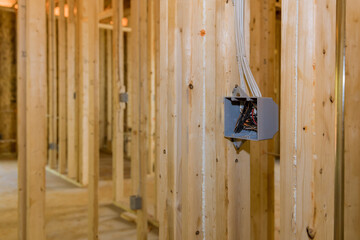 An electrical switch box plastic mounted wires on wooden frame beams on wall
