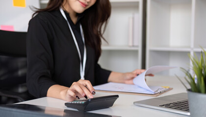 Close up Business woman using calculator and laptop for do math finance on wooden desk in office and business working background, tax, accounting, statistics and analytic research concept
