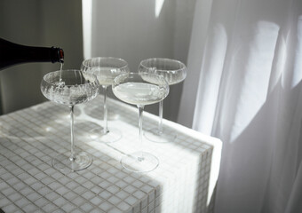 Champagne pourig into glasses on a light table surface reflecting soft sunshine rayson
