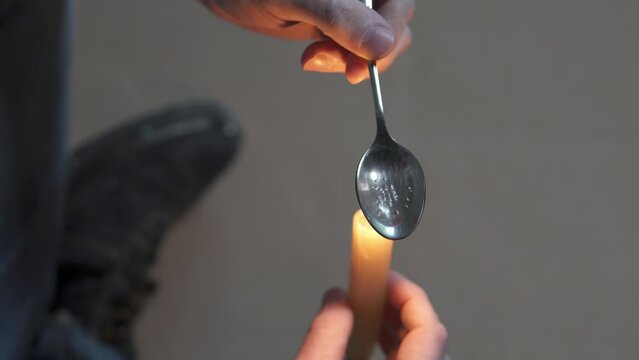 A drug addict cooks heroin on a spoon with the help of a candle fire. Drug addiction and homelessness concept.