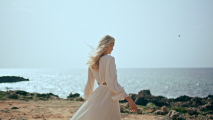 Fototapeta na wymiar Gentle woman relaxing coast at beautiful sunset light. Girl walking ocean shore