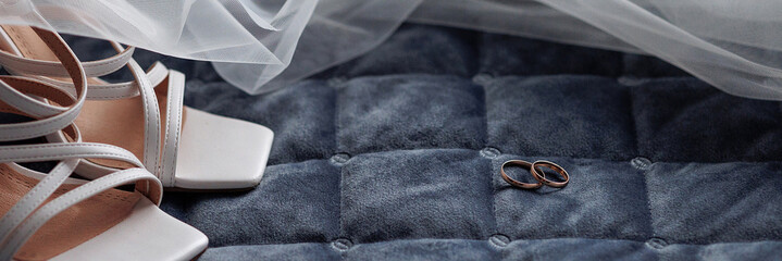 Two intertwined gold wedding rings resting on a blue quilted fabric. A white veil adds a touch of...
