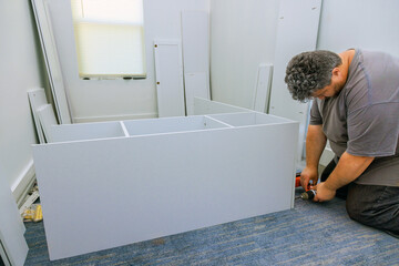 Carpenter uses screwdriver to assemble the furniture closet cabinet to room