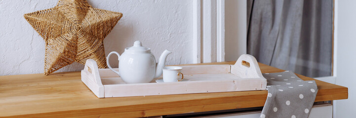 A white tea set neatly arranged on a wooden tray and countertop, creating a cozy and inviting atmosphere. Concept for home decor, hospitality, and tea time relaxation. Banner with copy space.