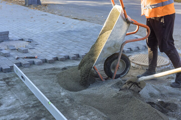 Using wheelbarrow to dump sand on footpath in preparation for laying decorative stones