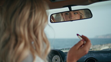 Sexy woman looking car mirror checking makeup closeup. Girl correcting hairstyle