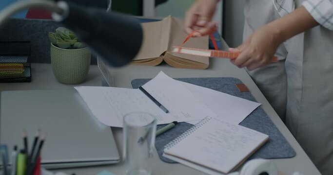 Close-up of female hands tidying desk holding books and stationery objects cleaning apartment. Modern lifestyle and housework concept.