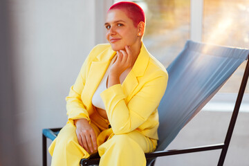 Beautiful relaxed woman in yellow suit  and red shot hair holding hand behind head
