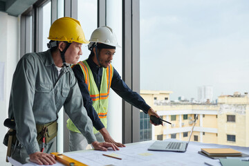 Construction workers looking at chart on laptop screen when discussing plan of building