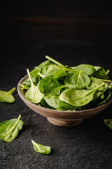 Fresh spinach leaves on dark boel on black background. Healthy vegan food.