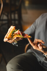 A piece of delicious pizza in hands on a dark background.