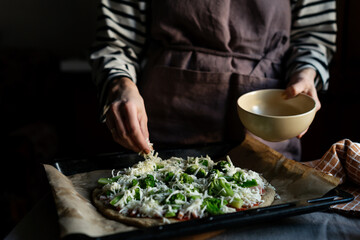 Woman preparing low carb and keto pizza at home. Almond flour dough filled with broccoli, tomato paste, ham and cheese