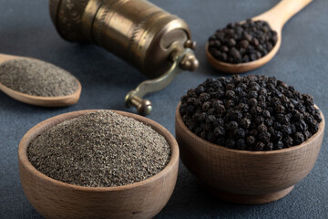 Black peppercorns, ground black pepper and metal mill on black background
