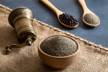 Black peppercorns, ground black pepper and metal mill on black background