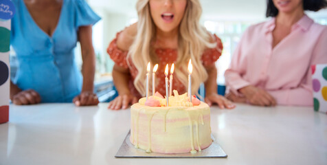 Mature Woman At Home Celebrating Birthday With Friends And Blowing Out Candles On Cake