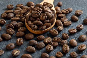 A spoon full of roasted coffee beans on black background