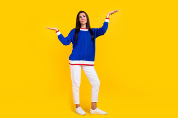 Full body photo of young latin woman in blue knit jumper weight two objects unsure looking advantages isolated on yellow color background