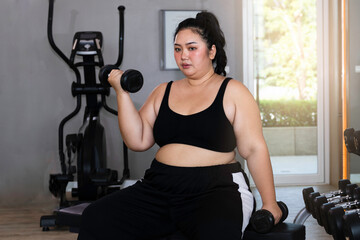 Fototapeta na wymiar Overweight Asian woman in sports clothes exercising by lifting dumbbells with her arms in the gym.