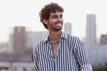 An attractive curly-haired guy in a striped shirt smiles against the backdrop - obrazy, fototapety, plakaty