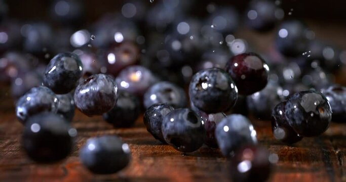 Super slow motion of green dietetic organic fresh blueberries fruits are falling on rustic wooden table of restaurant.