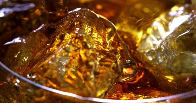 Super slow motion macro of old malt bourbon whiskey is poured in cocktail with ice cubes in transparent glass is being mixed by bartender in bar or club.
