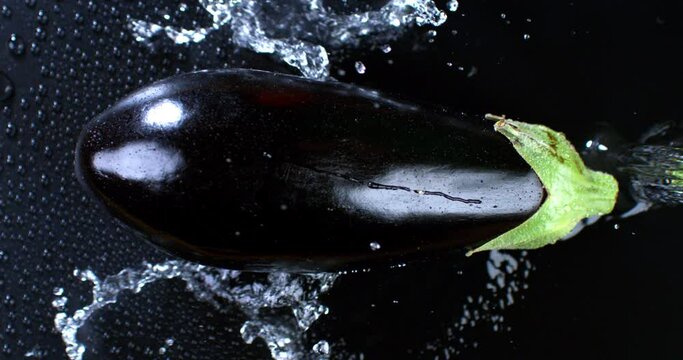 Super slow motion of water drops are falling with splashing on green dietetic organic fresh eggplant vegetable isolated soft dark background 1000 fps.