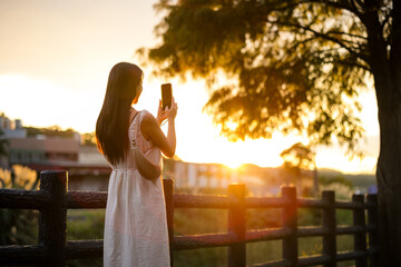 Woman use of mobile phone to take photo under sunset