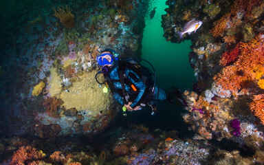 A female scuba diver swimming through a swim-through on the deep reef underwater