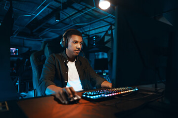 Gamer engrossed in play at a backlit keyboard setup. Concentrated player in a dim gaming...