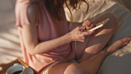 Female hands typing smartphone in bed closeup. Cozy breakfast coffee in bedroom
