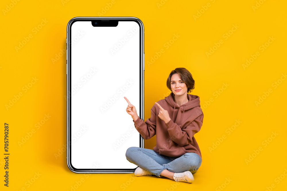 Poster Full body size photo of young girl pointing finger empty space nomad phone touchscreen wear sweatshirt isolated on yellow color background