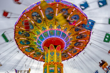 Um brinquedo grande e colorido no parque de diversões com poucas pessoas, em um dia nublado. Foto feita de baixo para cima. - obrazy, fototapety, plakaty