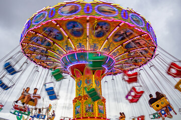 Detalhe de um brinquedo gigante de rotação no parque de diversões com poucas pessoas, rodando em baixa velocidade, em um dia nublado. Foto feita de baixo para cima.