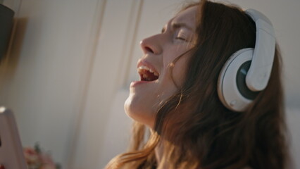 Happy girl singing headphones at home closeup. Energetic pretty female dancing