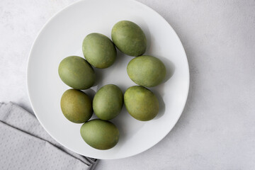 Green eggs in a white plate on a light background. Minimal concept. View from above. Easter eggs. Photos of preparations for Easter.