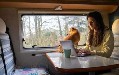 Woman teleworking while traveling in a motorhome with the computer and in the company of her dog