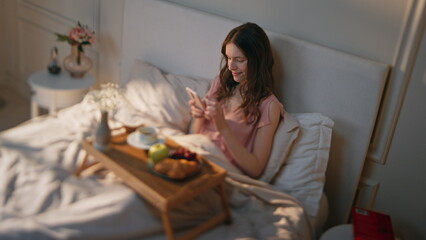Serene woman texting mobile phone in morning. Relaxed girl enjoying breakfast - obrazy, fototapety, plakaty
