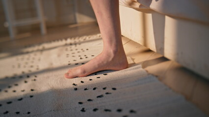 Woman legs stepping bed in sunlight closeup. Unknown woman wake up early morning