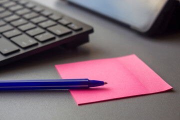 A blue pen lying on a pink sticky note beside a computer keyboard