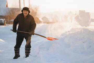Elderly man cleaning snow with shovel after snowstorm, sunlight