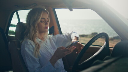 Woman driver texting telephone sitting retro car close up. Blonde focused screen