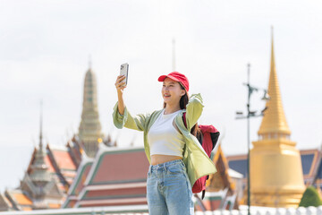 Young asian woman traveler with phone capturing moments and exploring Wat Phra Kaew and The Grand...