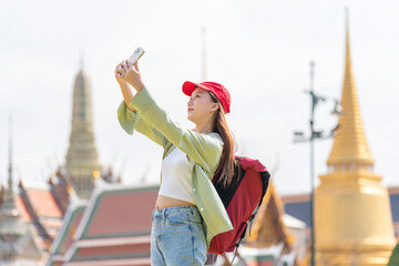 Young asian woman traveler with phone capturing moments and exploring Wat Phra Kaew and The Grand...