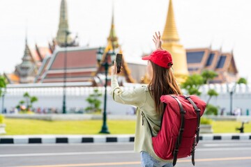 Naklejka premium Young asian woman traveler with phone capturing moments and exploring Wat Phra Kaew and The Grand Palace in a happy and casual style during a sunny day