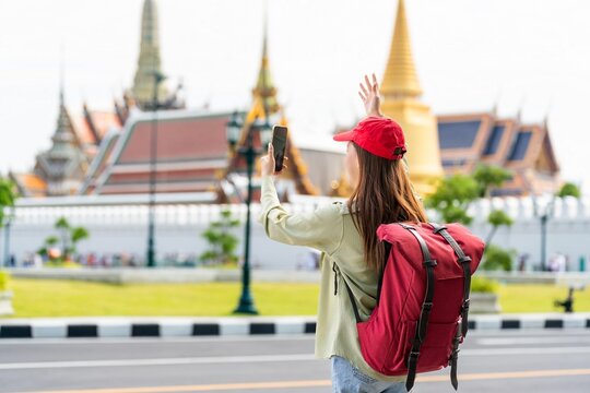 Young asian woman traveler with phone capturing moments and exploring Wat Phra Kaew and The Grand Palace in a happy and casual style during a sunny day