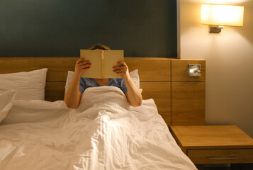 Middle age caucasian woman reading book sitting on the bed at bedroom